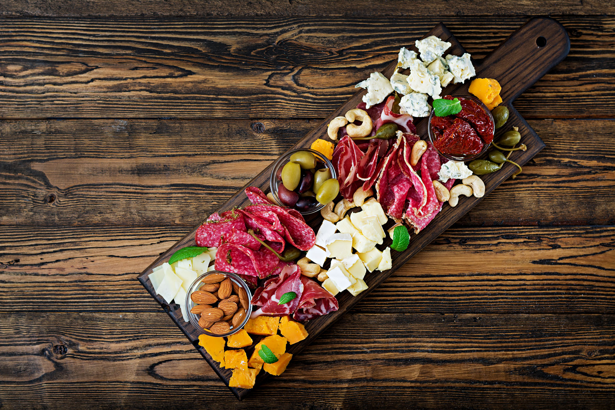 A wooden platter with various meats and cheeses.