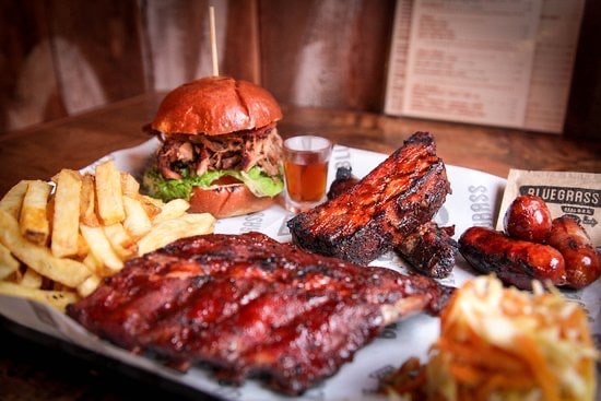 A large plate of barbecued meats, burger, fries, and a side